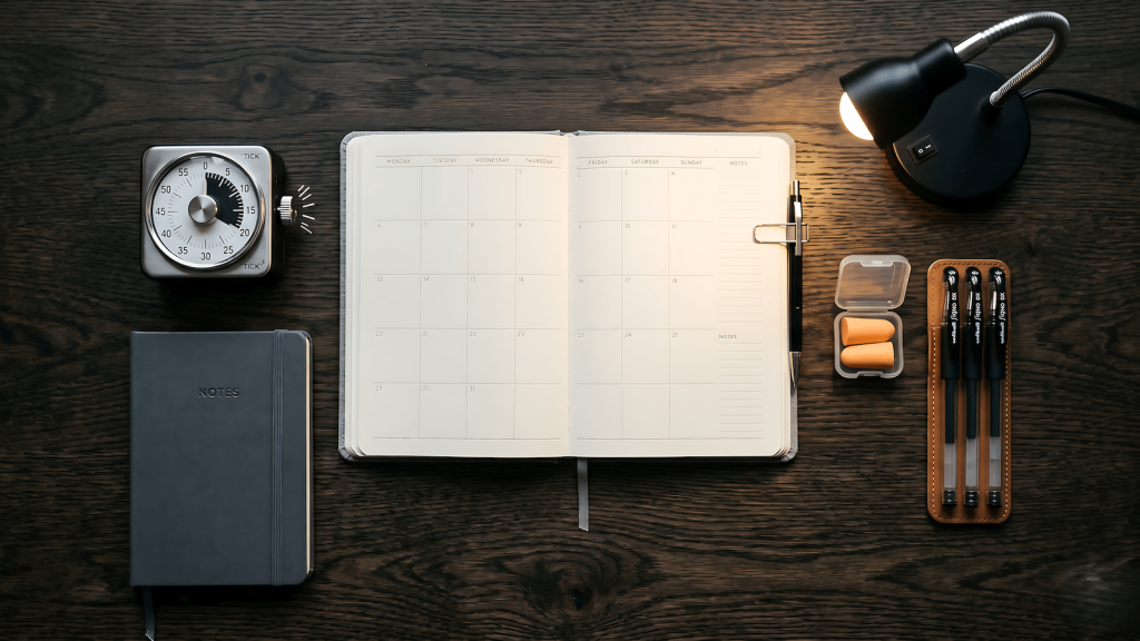 Budget productivity setup on a dark desk with analog timer, planner, notebook, and earplugs